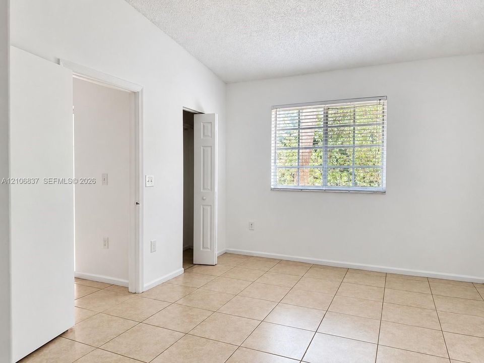 Neutral-toned ceramic tile flooring, crisp white walls, and a window featuring horizontal blinds
