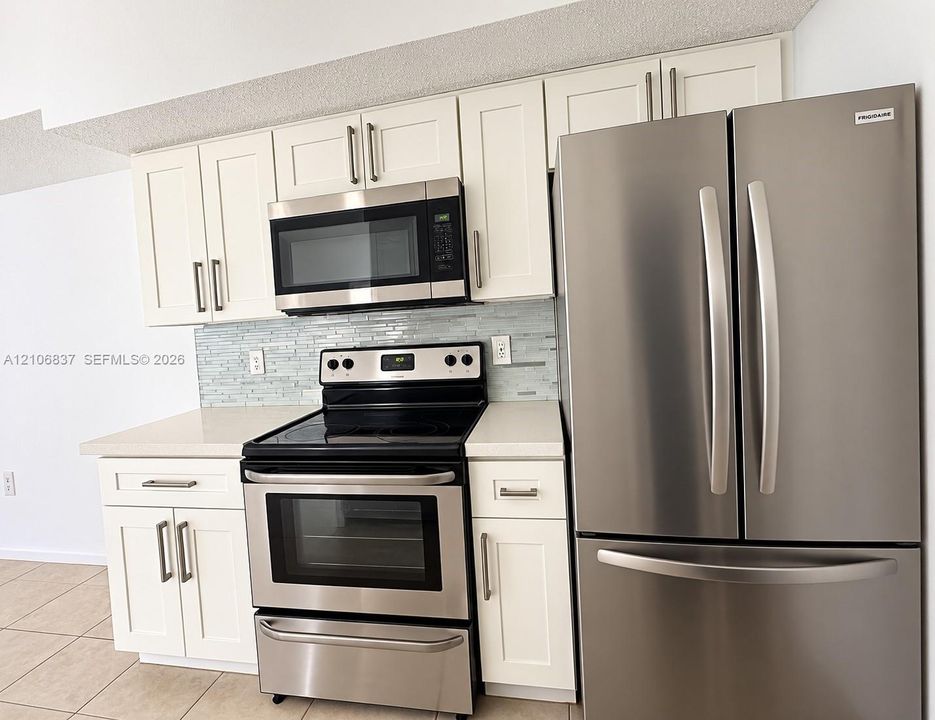 Kitchen featuring white shaker-style cabinetry, stainless steel appliance suite, quartz countertops, and a glass-tile backsplash