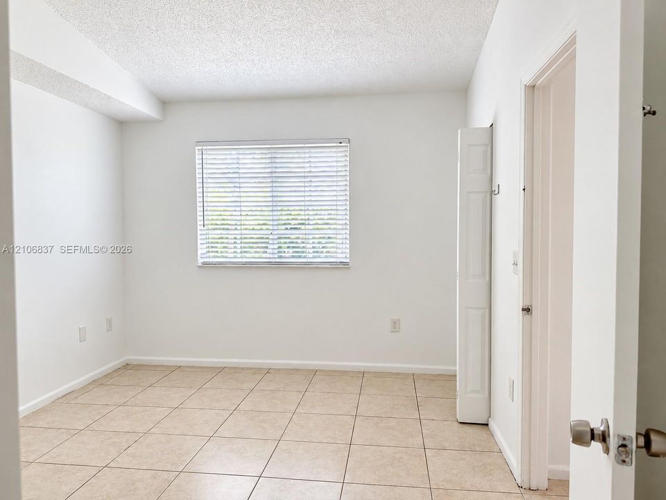 Neutral-toned ceramic tile flooring, horizontal window blinds, and bi-fold closet doors