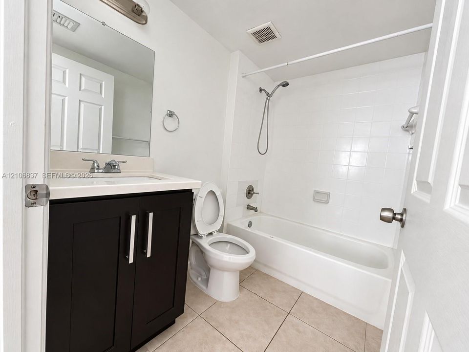Bathroom featuring a dark-finish vanity with a light-toned countertop, ceramic tile flooring, and a tub-shower combination with a handheld fixture