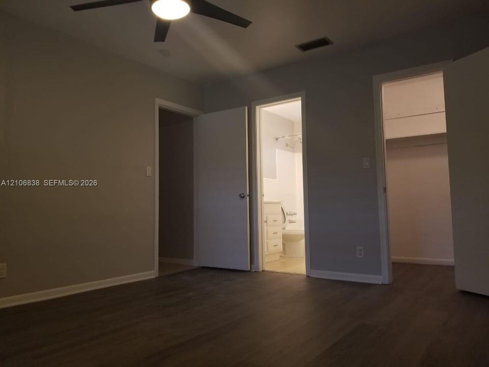 Room featuring wood-finish flooring, a ceiling fan with integrated lighting, and dual doorways leading to a bathroom and a closet with built-in shelving