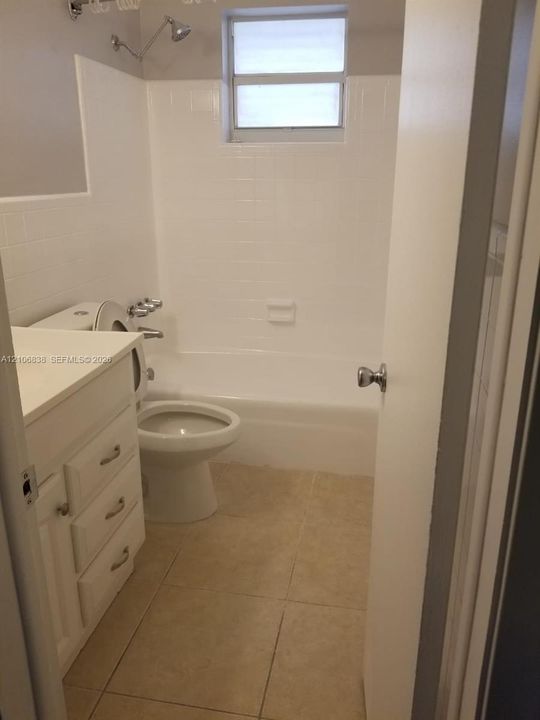 Bathroom featuring a white vanity with integrated basin, tiled shower-tub combination, ceramic floor tile, and a wall-mounted shower fixture
