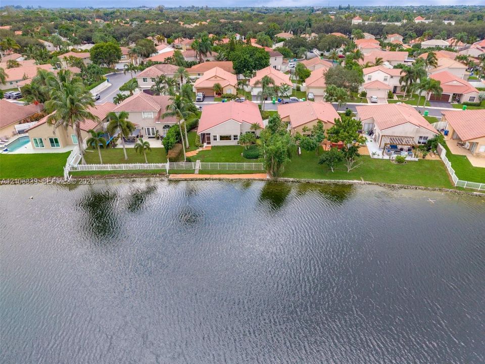Waterfront residential property featuring a manicured lawn, white perimeter fencing, and mature palm trees