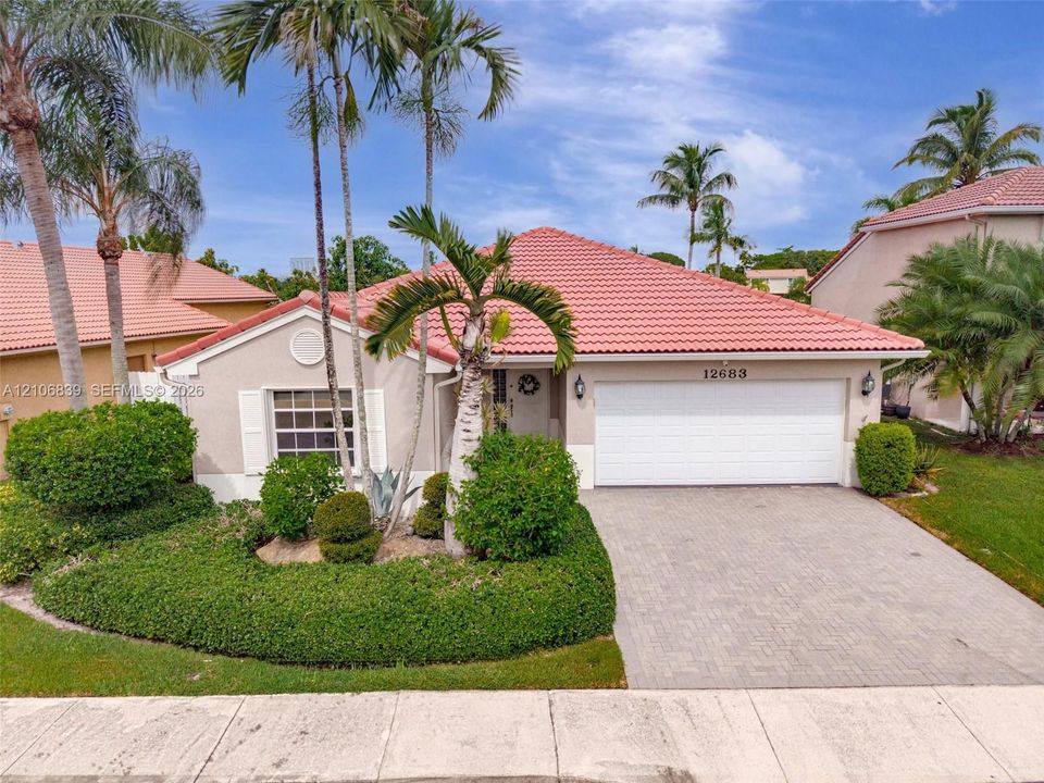 Single-story residence featuring a terracotta-tiled hip roof, stucco facade, paved driveway, two-car garage, and established landscaping