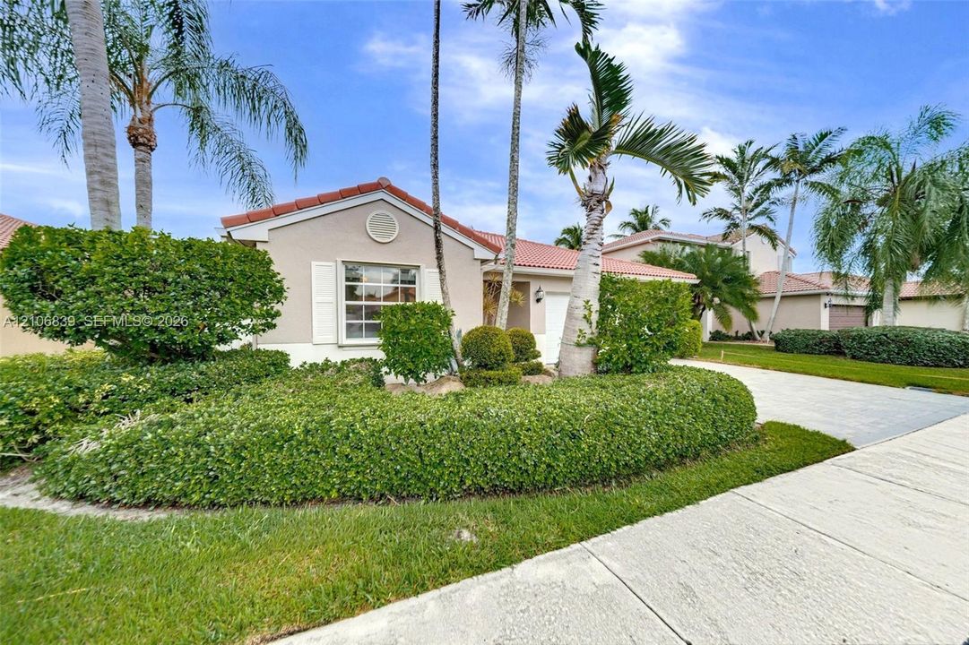 Exterior facade featuring a tile roof, stucco siding, and a paved driveway, complemented by mature landscaping and palm trees