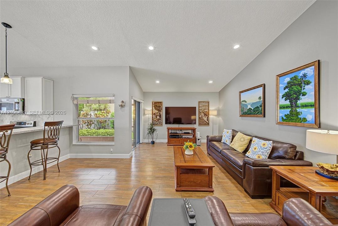Open-concept living space featuring vaulted ceilings, recessed lighting, wood-finish tile flooring, white cabinetry, and sliding glass doors