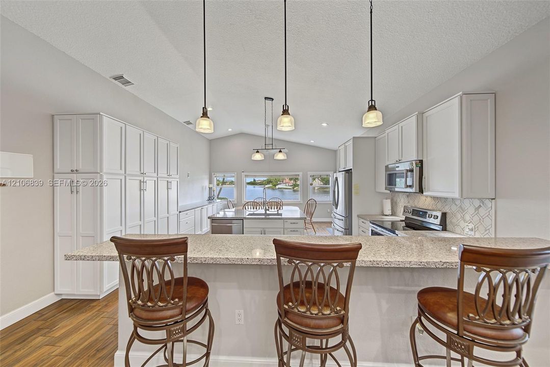 Kitchen featuring a vaulted ceiling, quartz countertops, white cabinetry, three pendant lights, and wood-finish flooring