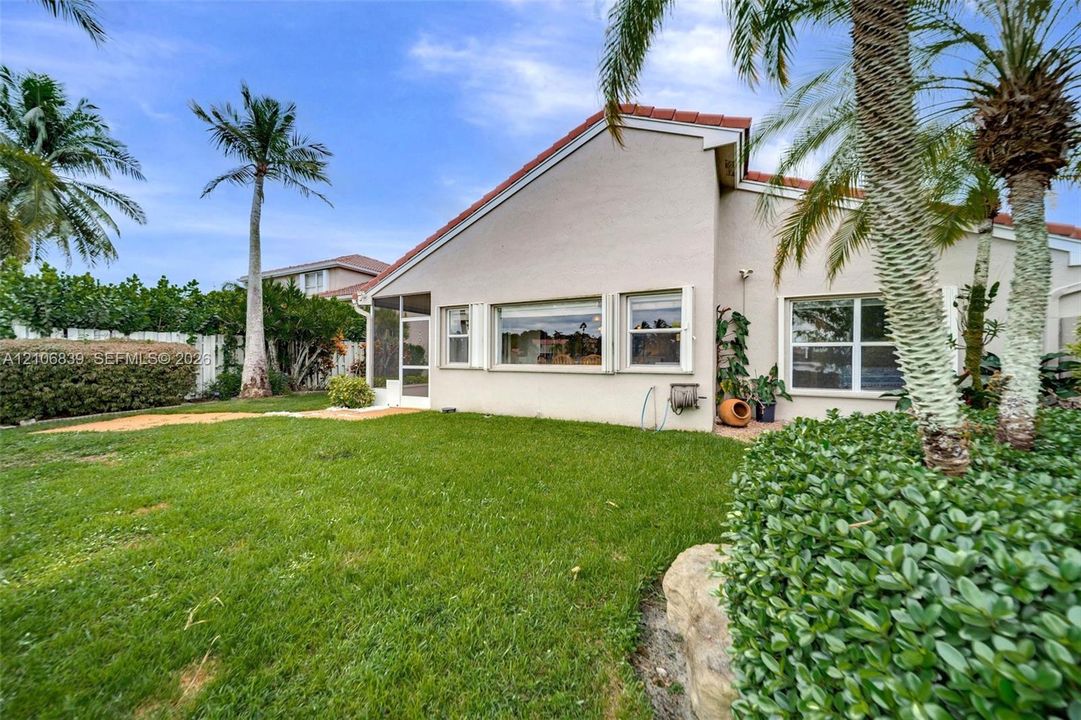 Exterior featuring a stucco facade, red tile roof, screened-in entry, and mature palm trees within a grass lawn