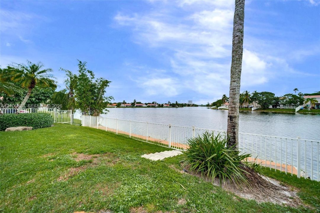 Waterfront backyard featuring a manicured lawn, perimeter metal fencing, and mature palm trees