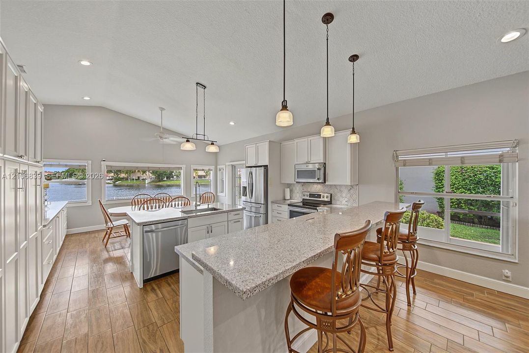 Kitchen featuring wood-finish flooring, quartz-surround island with breakfast bar, stainless steel appliances, white cabinetry, and pendant lighting