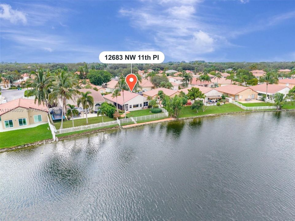 Waterfront residence featuring a tiled roof, screened-in patio, and manicured lawn with mature palm trees