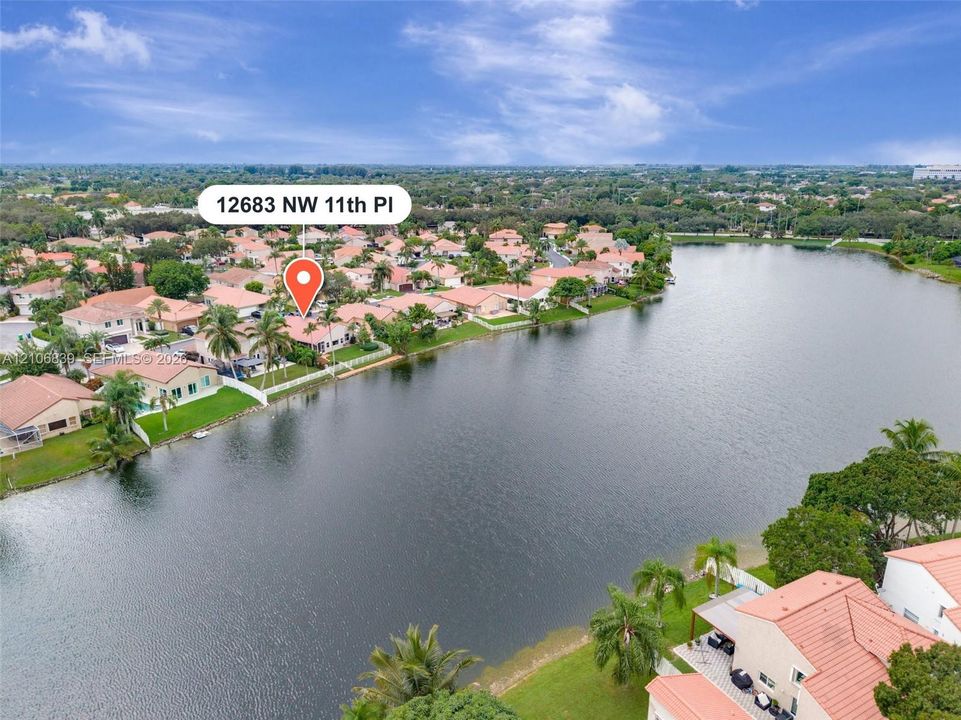 Waterfront property featuring tile roofing, mature palm trees, and manicured landscaping