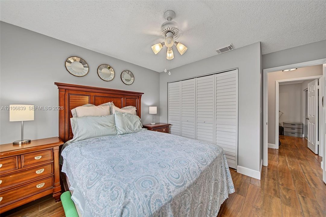 Wood-finish flooring, white louvered-panel closet doors, and a ceiling-mounted light fixture with a central fan
