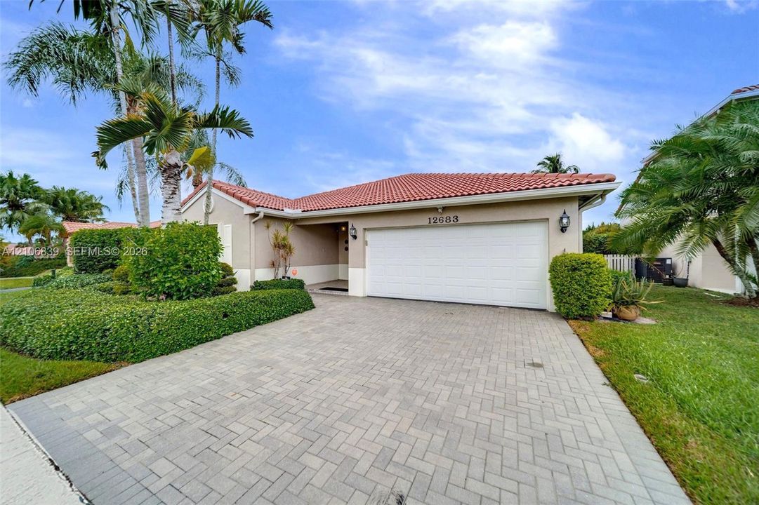 Exterior featuring a tile roof, paver driveway, two-car garage, and established landscaping with palm trees
