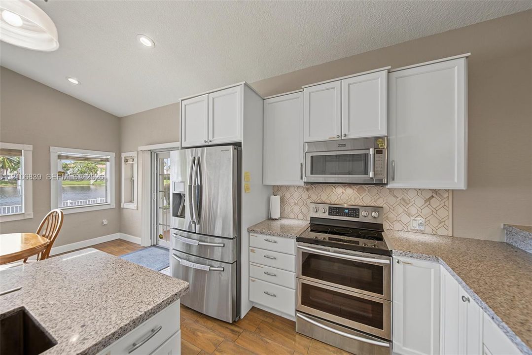 Kitchen featuring white cabinetry, stainless steel appliances, speckled stone-finish countertops, geometric-patterned backsplash, and wood-finish tile flooring