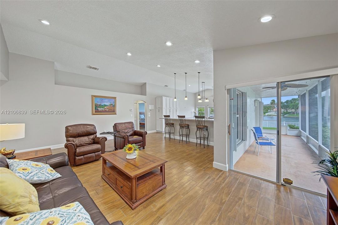 Open-concept interior featuring wood-finish tile flooring, recessed lighting, breakfast bar with pendant lighting, and sliding glass doors leading to a screened-in patio