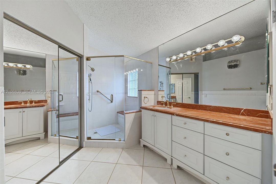 Bathroom featuring white cabinetry, stone-finish countertops, a glass-enclosed shower, tile flooring, and wall-to-wall mirrors