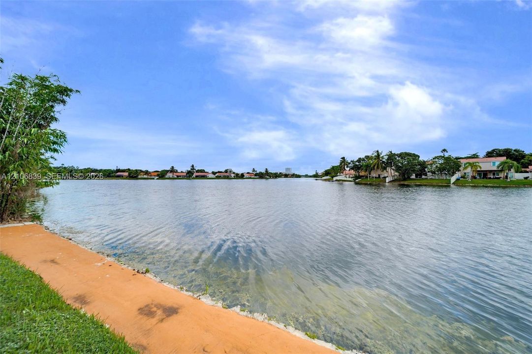 Waterfront property featuring a paved walkway, mature landscaping, and an expansive canal backdrop