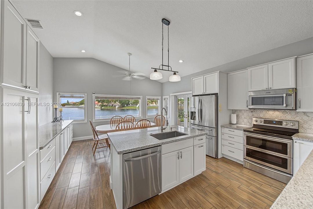 Kitchen featuring vaulted ceilings, wood-finish flooring, a central island with a stainless steel undermount sink, quartz countertops, and stainless steel appliances