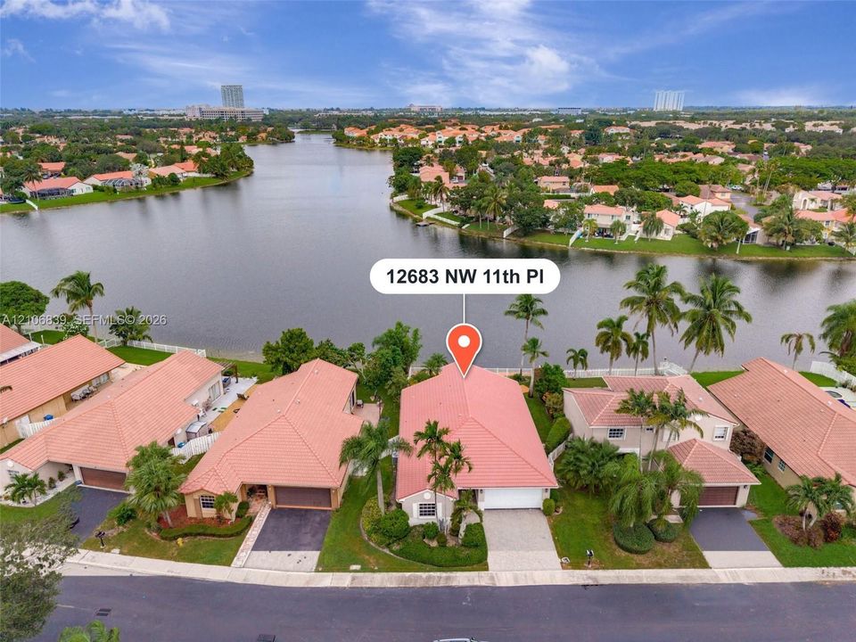 Waterfront property featuring a tile roof, paved driveway, two-car garage, and established palm landscaping