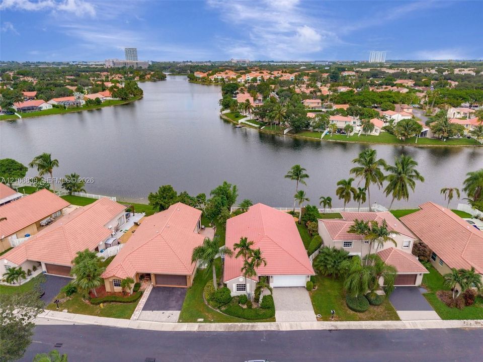 Aerial perspective of a waterfront residential enclave featuring terra-cotta tile roofs, paved driveways, manicured landscaping, and mature palm trees