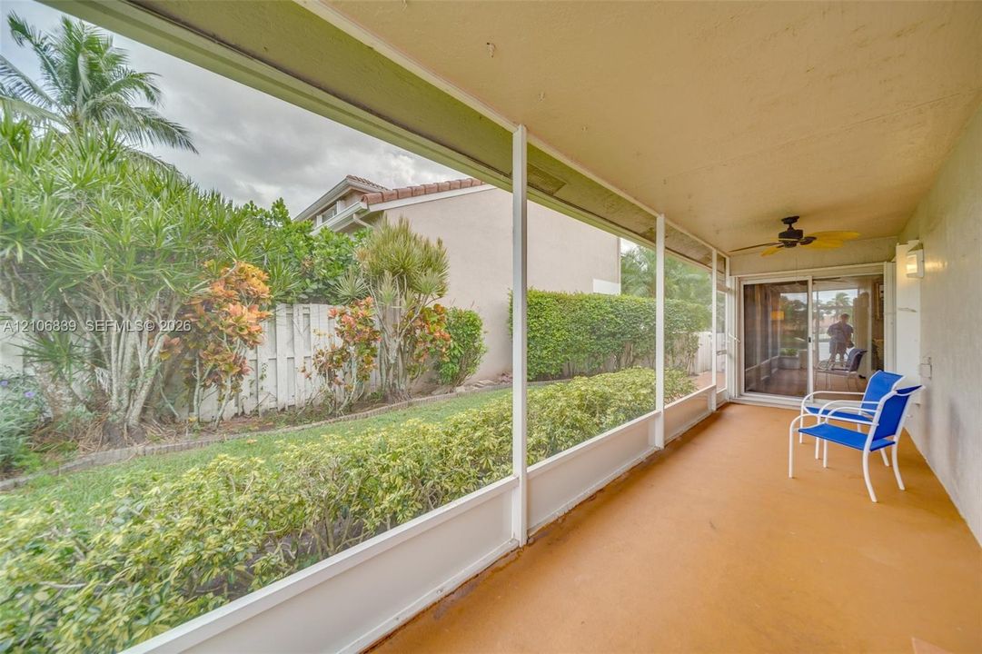 Screen-enclosed lanai featuring a solid concrete floor, ceiling fan, and sliding glass door entry