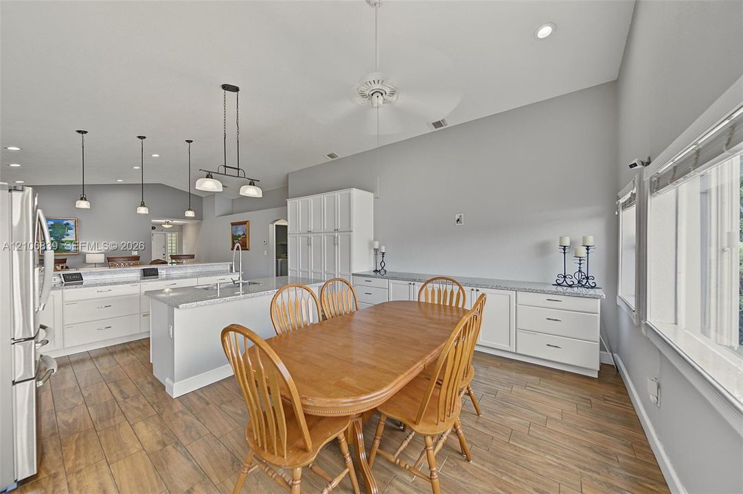 Open-concept kitchen featuring white cabinetry, stone countertops, wood-finish flooring, a central island with sink, and integrated overhead pendant lighting