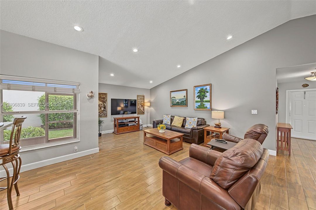 Living area featuring vaulted ceilings, recessed lighting, and wood-finish flooring