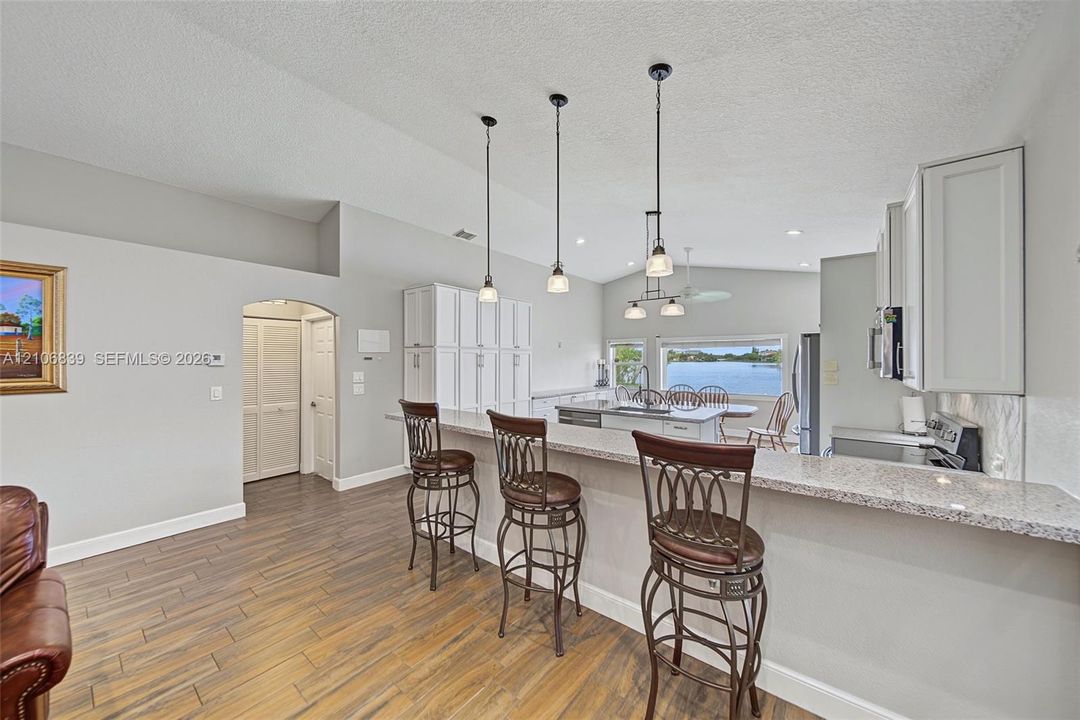 Kitchen featuring a tiered countertop, wood-finish flooring, white cabinetry, decorative pendant lighting, and water scenery