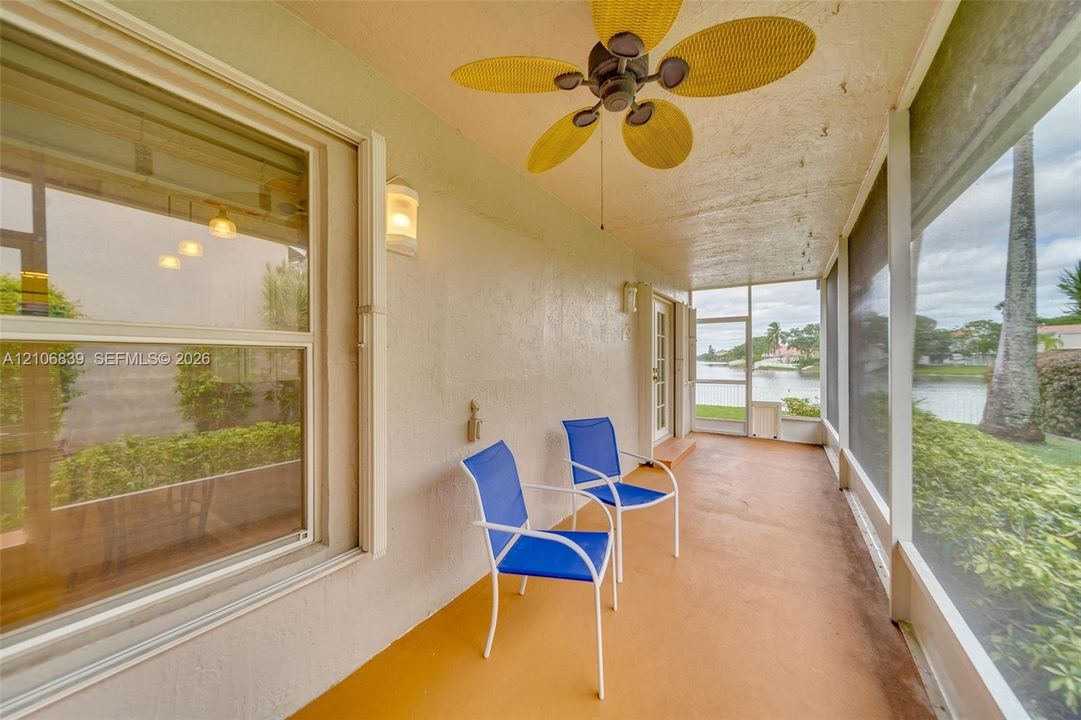 Screened-in porch featuring a textured ceiling, ceiling fan with paddle-style blades, dual wall-mounted light fixtures, and water frontage
