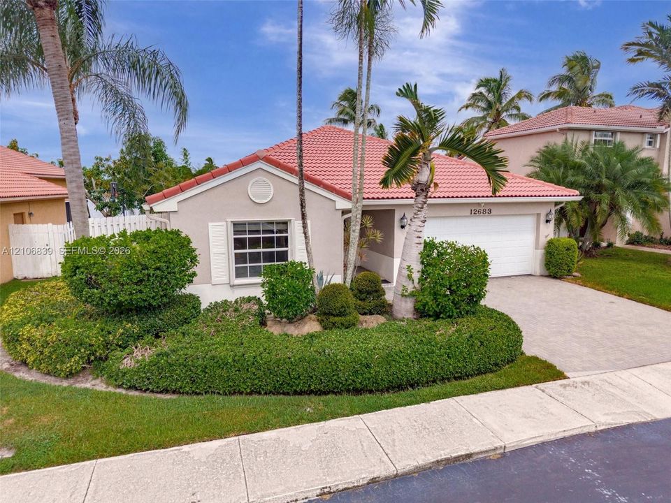 Stucco exterior featuring a terracotta-tile roof, paved driveway, window shutters, and established tropical landscaping