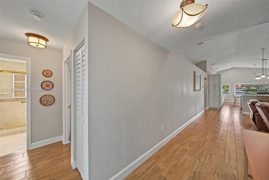 Interior hall featuring wood-finish tile flooring, vaulted ceilings, louvered closet doors, and decorative flush-mount ceiling light fixtures