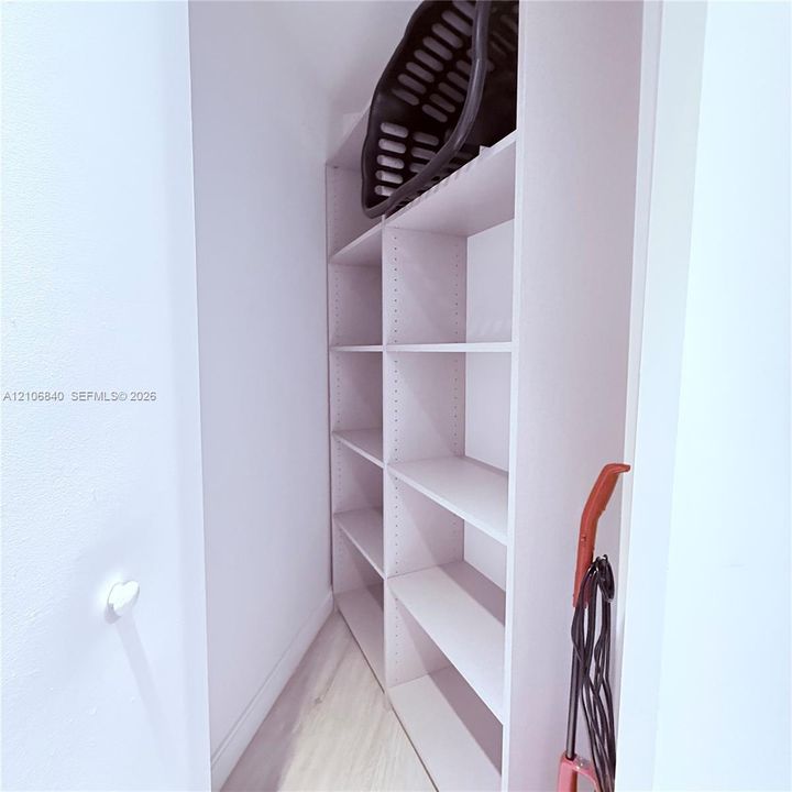 Built-in, floor-to-ceiling white shelving with adjustable cabinetry and light-toned wood-finish flooring