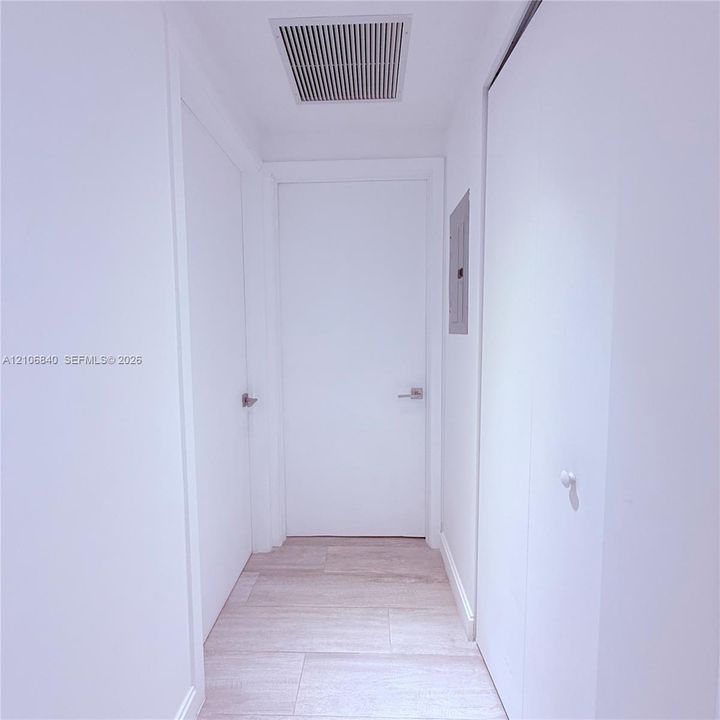 Hallway featuring light-toned wood-finish flooring, solid-core doors with brushed metal lever handles, and neutral wall finishes