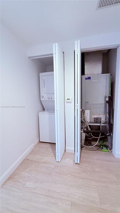 Utility closet featuring a stacked washer and dryer unit, HVAC equipment, and light-toned wood-finish flooring