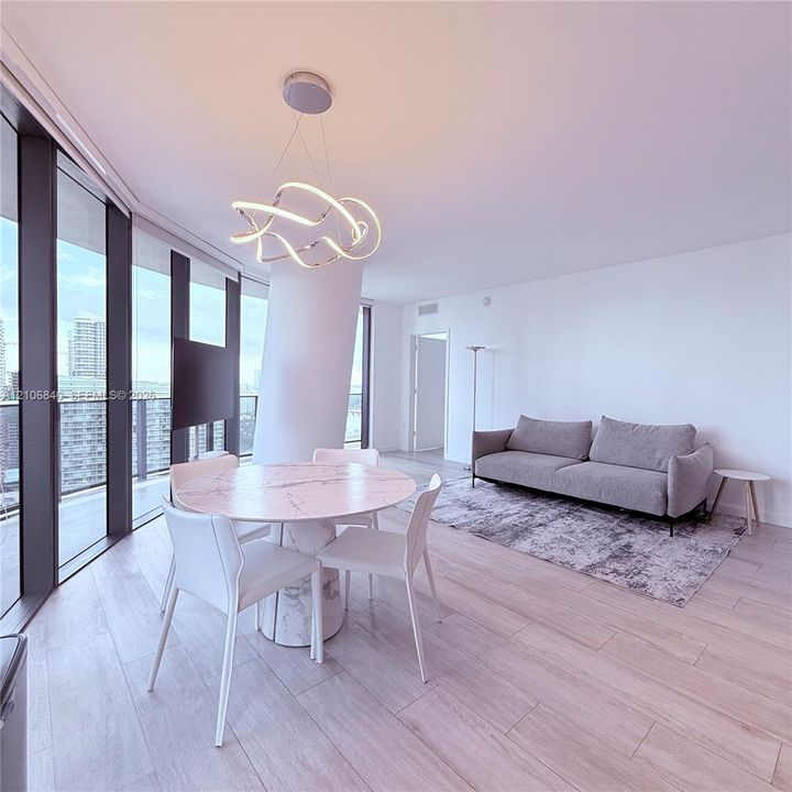 Floor-to-ceiling windows, wood-finish flooring, sculptural LED pendant lighting, and a neutral color palette