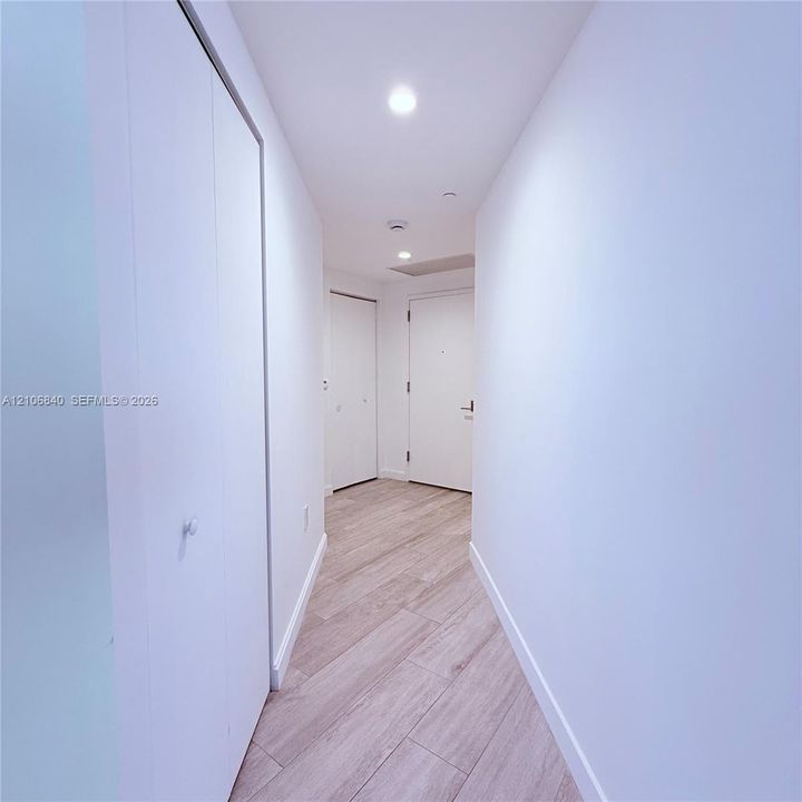 Hallway featuring wood-finish flooring, recessed lighting, and multiple interior closet doors with white hardware