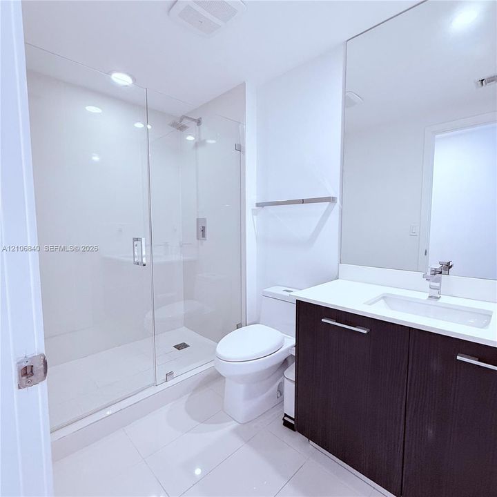 Bathroom featuring a glass-enclosed walk-in shower, dark-toned vanity with a light-colored countertop, integrated rectangular sink, and floor-to-ceiling mirror