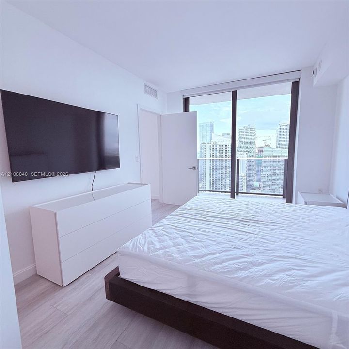 Floor-to-ceiling glass sliding doors, private balcony, wood-finish flooring, and neutral wall palette