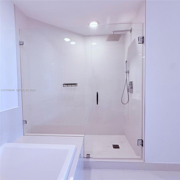 Walk-in shower featuring a frameless glass enclosure, rainfall showerhead, handheld shower attachment, integrated wall niche, and tile flooring