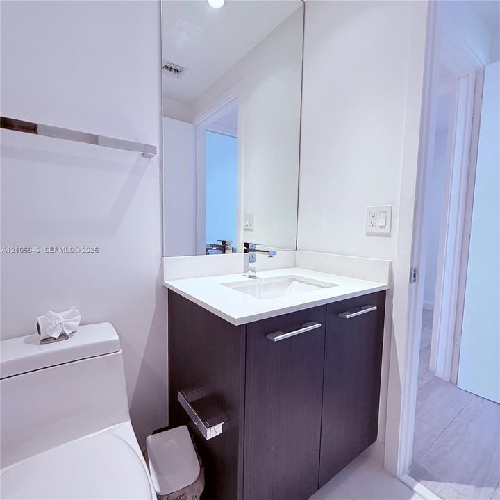 Bathroom featuring a vanity with a white countertop and rectangular undermount sink, chrome faucet, full-height wall mirror, and dark-finish cabinetry with metallic hardware