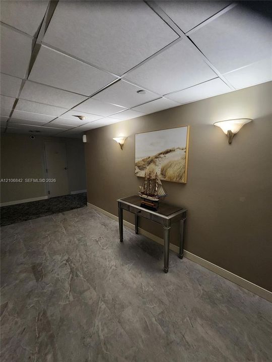 Large-format stone-tile flooring and recessed drop-ceiling grid with integrated wall-mounted sconce lighting