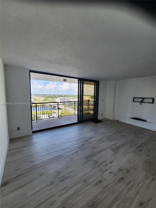 Open-concept living space featuring wood-finish flooring, floor-to-ceiling sliding glass doors, and a covered balcony with metal railing