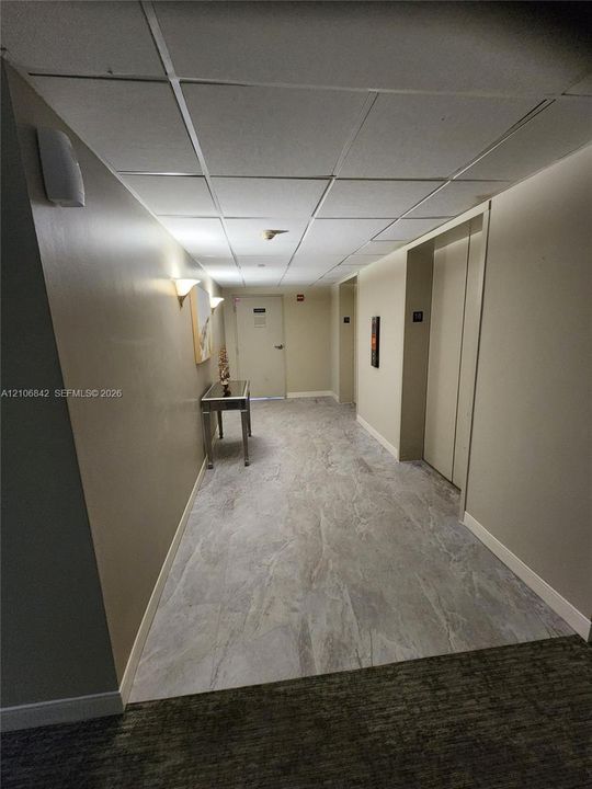 Hallway featuring a drop-tile ceiling, neutral-toned wall paint, and stone-finish tile flooring