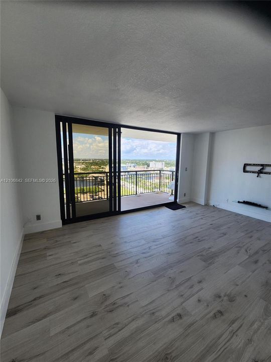Living area featuring wood-finish flooring, floor-to-ceiling sliding glass doors, and a private balcony with metal railings