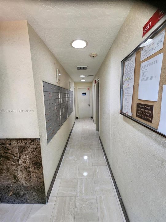 Interior corridor featuring stone-finish floor tiling, wall-mounted mail lockers, recessed lighting, and decorative stone-textured wall accents