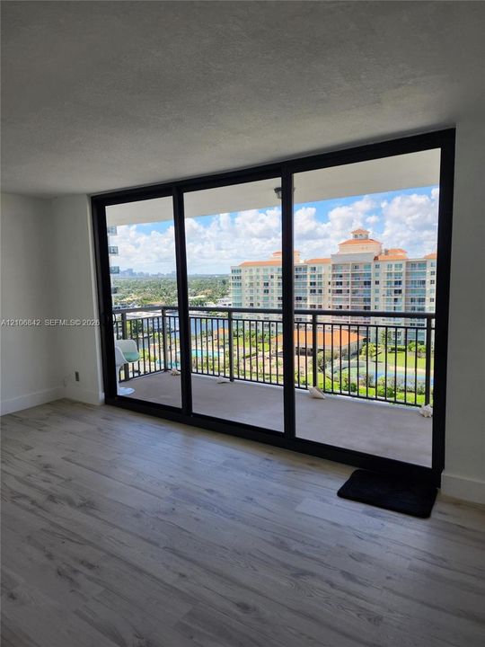 Floor-to-ceiling glass sliding doors opening to a covered balcony with metal railings and light-toned wood-finish flooring