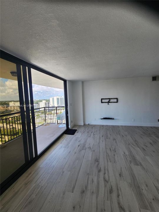 Floor-to-ceiling sliding glass doors, private balcony with metal railing, and wood-finish flooring