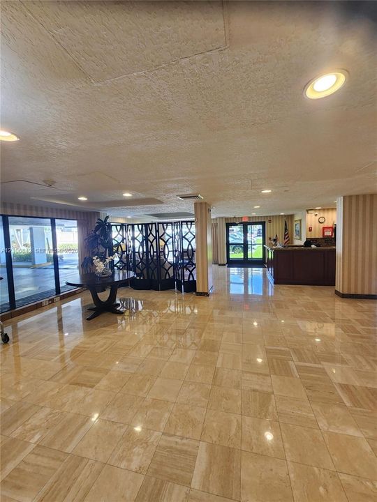 Lobby featuring polished stone tile flooring, recessed lighting, floor-to-ceiling glass windows, and a built-in wooden reception desk