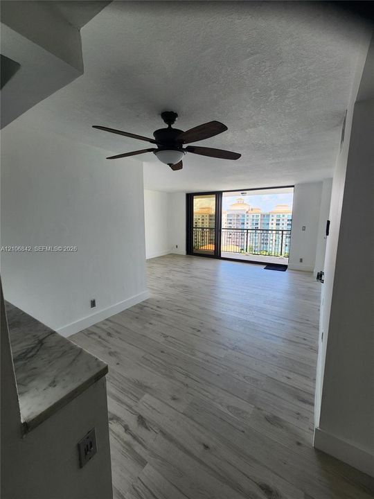 Light-toned wood-finish flooring, stone-surfaced counter, ceiling fan with integrated lighting, and full-height sliding glass doors leading to a balcony